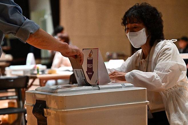 투표 참관인의 감독 하에 한 유권자가 투표 용지를 투표함에 넣고 있다