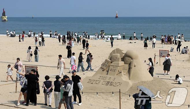 21대 대통령 선거일이자 초여름 날씨를 보인 3일 오후 부산 해운대해수욕장에 설치된 대통령 선거 홍보 모래작품 뒤로 시민, 관광객 등이 더위를 식히고 있다. 2025.6.3/뉴스1 ⓒ News1 윤일지 기자