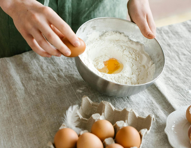 밀가루에 계란을 깨서 넣고 있는 손