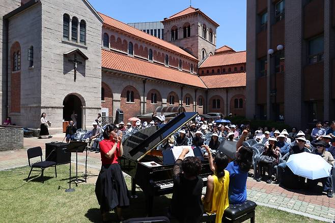 최은경(맨 앞 앉은 이 왼쪽부터), 강은하, 오정선 연주자가 2025년 6월4일 서울 중구 정동 대한성공회 서울대성당 마당에서 하나의 피아노로 ‘세비야의 이발사 서곡\' 연주를 마치며 손을 들어 올리고 있다.