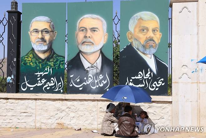 예멘에서 열린 후티 지지 집회 현장 근처에 걸려있는 하마스 지도부 초상화 (사나 EPA=연합뉴수) 13일(현지시간) 예멘 사나에서 후티 지지자와 아이들이 거리에 걸린 하마스 지도부의 초상화 사진 앞에서 휴식을 취하고 있다. 2025.06.15