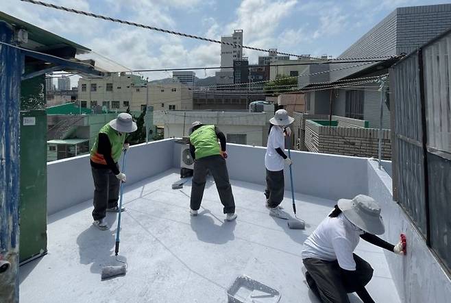한국주택금융공사 직원들이 대학생 봉사단과 옥상에 열차단 페인트 칠을 하고 있다.