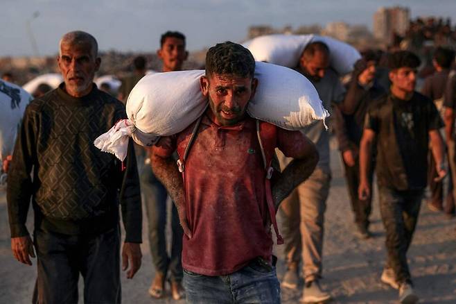 17일(현지시각) 구호품이 들어 있는 트럭이 가자지구에 진입하자 밀가루 포대를 든 사람들이 가자 북부 자발리야의 라시드 거리를 걷고 있다. 자발리야/AFP 연합뉴스