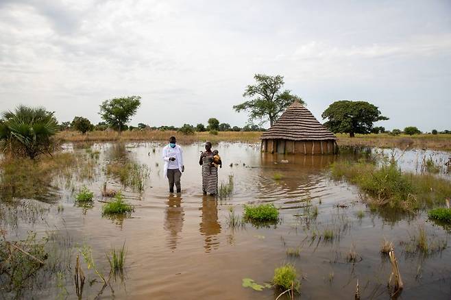 지난 2021년 10월 16일 남수단 바르엘가잘에서 일어난 홍수로 침수된 투쿨 마을에서 국제구조위원회 직원과 함께 서 있는 아부크와 네 살배기 딸 니루. 국제구조위원회 제공