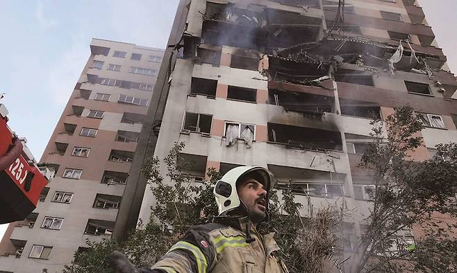 지난 6월 13일(현지시각) 오전 이스라엘 공군의 공습으로 파괴된 이란 수도 테헤란의 아파트에 출동한 소방대원이 동료에게 도움을 요청하고 있다. /사진 AP연합