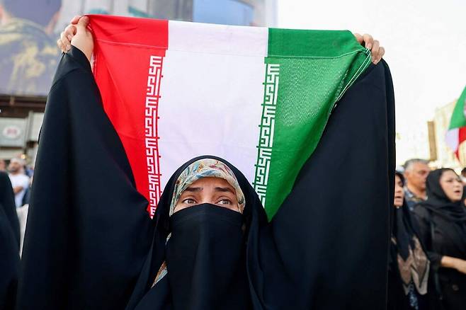 2025년 6월22일(현지 시각) 이란 테헤란의 엥헬랍 광장에서 열린 미국의 이란 공격에 항의하는 집회에서 한 이란 여성이 국기를 들어 보이고 있다. AFP 연합뉴스