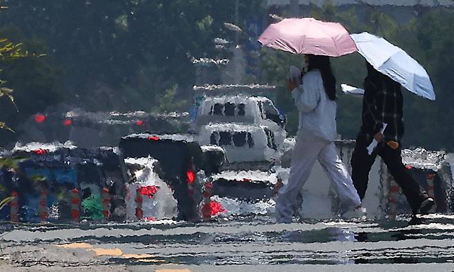 대구에 일주일째 폭염특보가 발효 중인 3일 대구 달서구 계명대학교 인근 도로에 지열로 인한 아지랑이가 피어오르는 가운데 시민들이 양산을 쓰고 이동하고 있다. 대구=연합뉴스