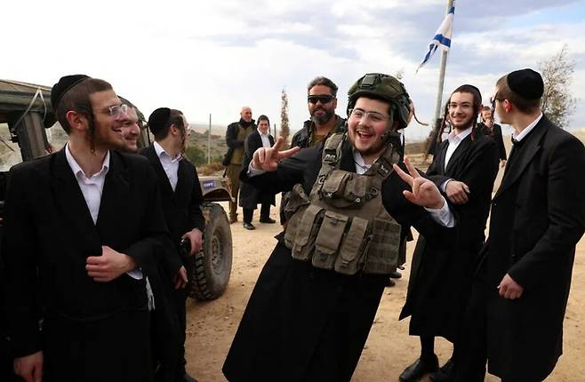 올해 1월5일(현지시각) 이스라엘 남부 도시 스데로의 한 언덕에서 군모와 탄약을 운반하는 군인으로부터 조끼와 헬멧 등을 빌려입은 이스라엘 초정통 유대인 남성이 동료들과 함께 웃고 있다. 스데로/AFP 연합뉴스