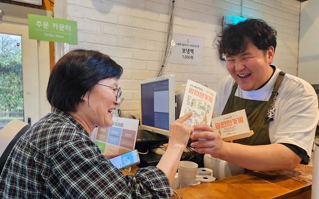 행복하게 사회적협동조합의 한 회원이 제주 애월읍에 있는 한 카페 점주에게 ‘맘편한 가게’를 인증하는 안내문을 전달하고 있다. 행복하게 사회적협동조합 제공