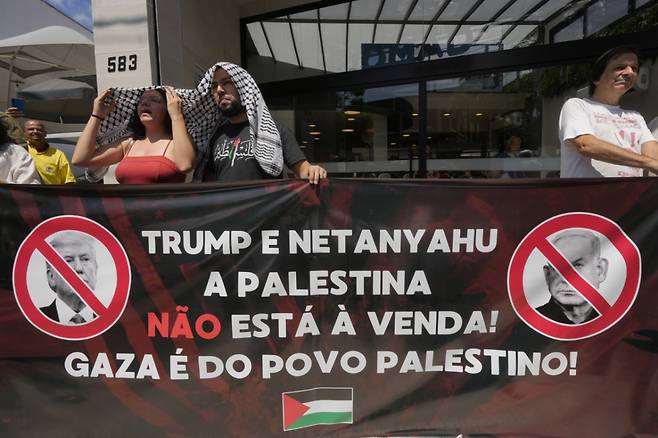 지난 2월 13일(현지 시간) 브라질 상파울루의 미국 총영사관 밖에서 친팔레스타인 시위대가 도널드 트럼프 미국 대통령의 팔레스타인인을 가자지구 밖으로 영구히 이주시키자는 제안과 해당 지역을 ‘중동의 리비에라’로 재개발하겠다는 구상에 반대하며 펼침막을 들고 있다. 이들이 들고 있는 펼침막에는 "트럼프와 네타냐후! 팔레스타인은 판매 대상이 아냐. 가자는 팔레스타인인의 것"이라고 쓰여 있다./AP=뉴시스