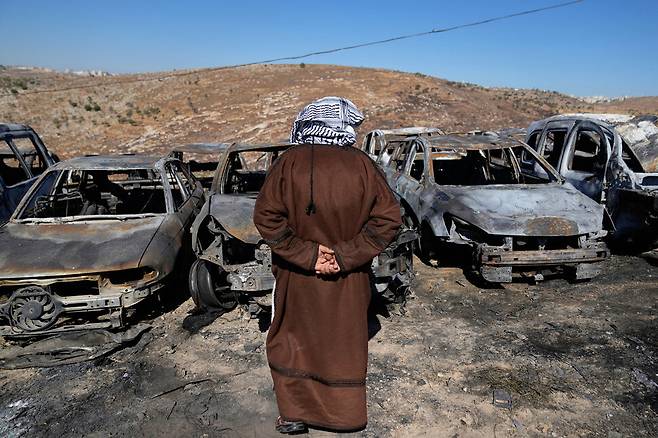 74살의 서안지구 주민 세이버 아사예가 15일(현지시각) 팔레스타인 자치정부 임시행정수도 라말라 동쪽 마을 부르카에 이스라엘 정착민들의 공격으로 밤새 불에 탄 차량들 앞에 서 있다.