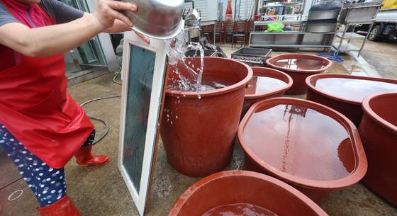 지난 21일 경남 산청군 신안면의 한 식당에서 식당 관계자가 공급받은 물로 흙탕물이 묻은 창문을 씻고 있다. 식당 관계자는 "호우 여파로 단전, 단수, 가스 공급이 중단됐고, 선풍기 돌릴 전기를 위층에서 끌어다가 쓰는 중이다"고 설명했다. 연합뉴스