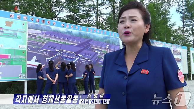 지난 18일 조선중앙TV 방송 화면 갈무리. 선전음악단원이 발언하는 모습 뒤로 '삼지연 국제비행장 복합형 역사 배치 계획안과 조감도'가 보인다.(조선중앙TV 갈무리).