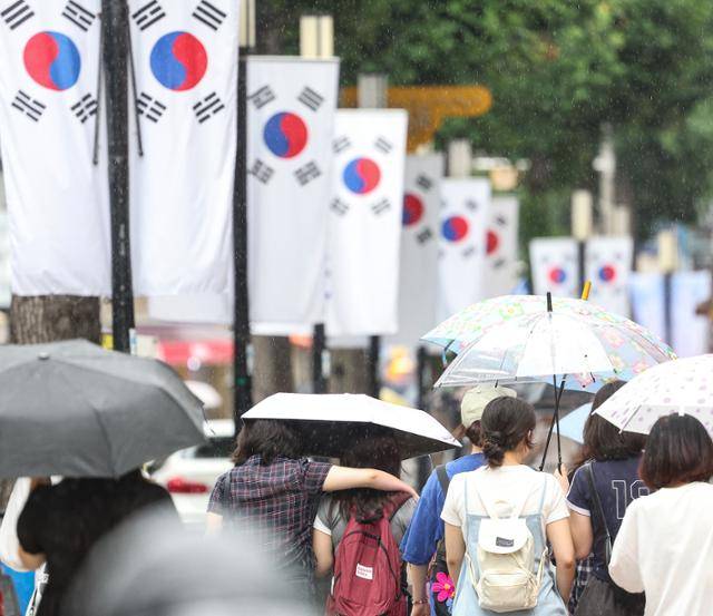 대구에 비가 내린 12일 대구 중구 동성로에 광복절을 앞두고 태극기가 게양된 가운데 시민들이 우산을 쓰고 이동하고 있다. 연합뉴스