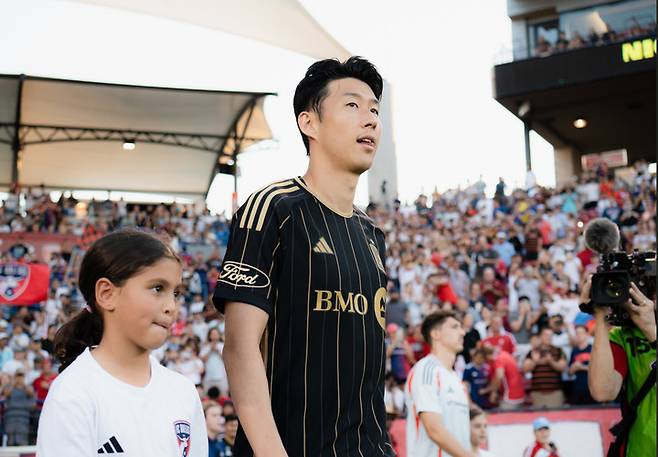 (손흥민이 어린이의 손을 잡고 달라스 원정경기를 치르기 위해 이동하고 있다)