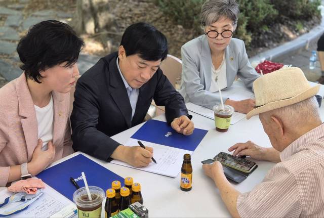 ▲30일 전주 서신길공원에서 열린 ‘이심전심 소통의 날’. 한 어르신이 딸의 훈장증 사진을 휴대폰으로 보여주며 불편함을 호소하자, 이성윤 의원(가운데)이 경청하며 메모하고 있다. ⓒ프레시안(양승수)