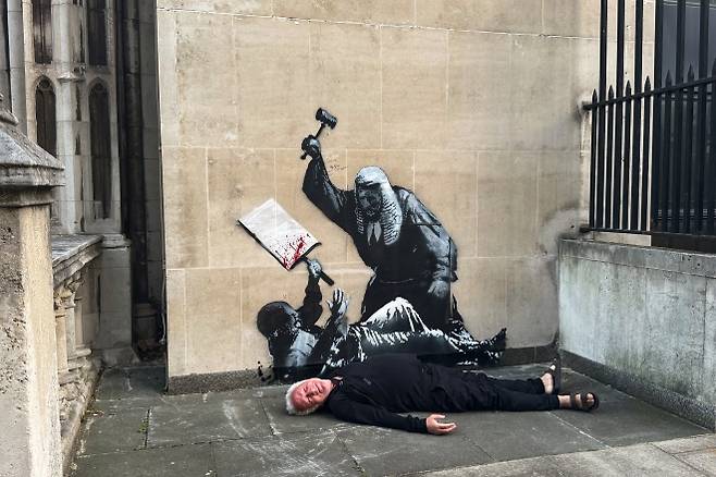 영국 런던 왕립법원 외벽에 등장한 뱅크시의 새 벽화 앞에 한 시민이 누워 있다. 2025년 9월 8일 촬영. 로이터 연합뉴스