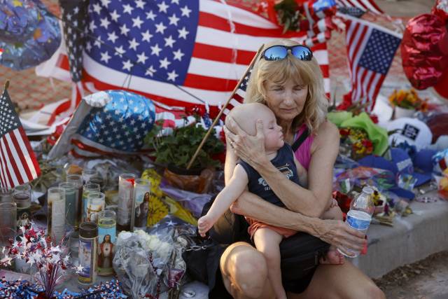 우파 정치 활동가 찰리 커크가 10일(현지 시간) 미국 애리조나주 피닉스에서 사망한 후 그가 운영하던 보수 단체 터닝포인트 본사 밖 임시 추모소에 한 여성이 아이를 안고 앉아 있다. EPA연합뉴스