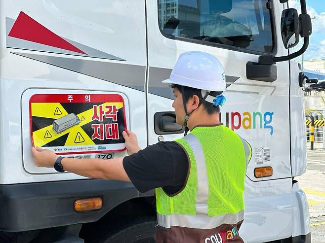 쿠팡로지스틱스서비스 관계자가 대형 화물차에 사각지대 주의 알림 표지를 부착하고 있다. 쿠팡 제공