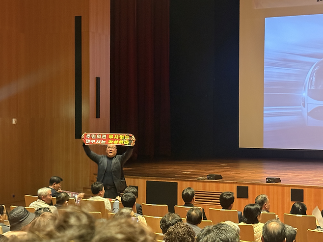 ▲ 31일 오후 북구 iM뱅크 제2본점에서 진행된 대구도시철도 4호선 주민설명회에서 한 주민이 현수막을 들고 항의하고 있다. 이유경 기자