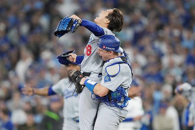 월드시리즈 우승을 확정하는 마지막 병살 타구를 유도한 뒤 모자를 벗고 포효하는 야마모토 요시노부(위쪽)와 그를 들어 올리며 축하하는 포수 윌 스미스. 토론토=AP 뉴시스