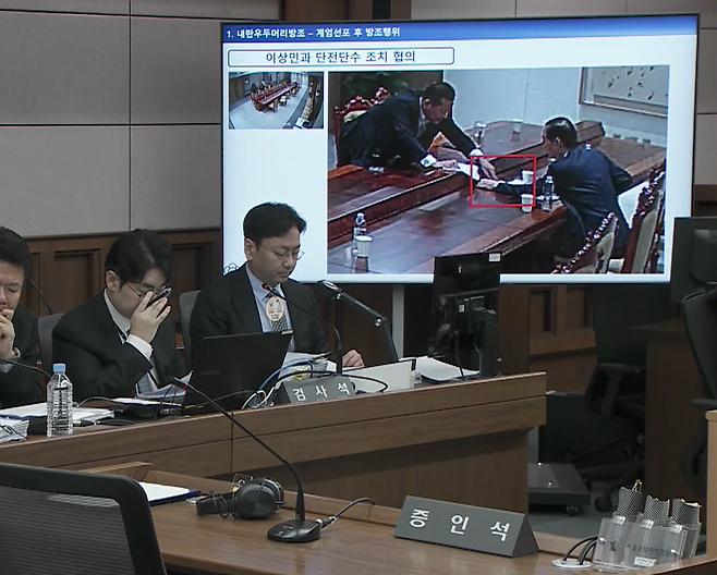 2025년 10월 13일 서울중앙지법 형사합의33부(부장판사 이진관) 심리로 열린 한덕수 전 국무총리 2차 공판에서 특검이 제시한 12·3 비상계엄 당일 대통령실 폐쇄회로(CC)TV 영상 화면에 한 전 총리(오른쪽)와 이상민 전 행정안전부 장관이 계엄 관련 문건을 주고받고 있는 모습이 재생되고 있다. 법원 공판 중계 화면 캡처