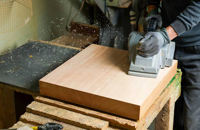 재단된 원목을 평평하게 대패로 깍아내고 있다.