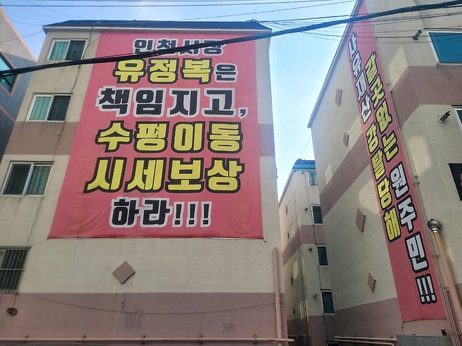 ▲ 제물포역 북측 도심 공공주택 복합사업 사업지구 내 한 5층짜리 아파트 벽면에 걸린 반대 현수막. /유희근 기자 allways@incheonilbo.com