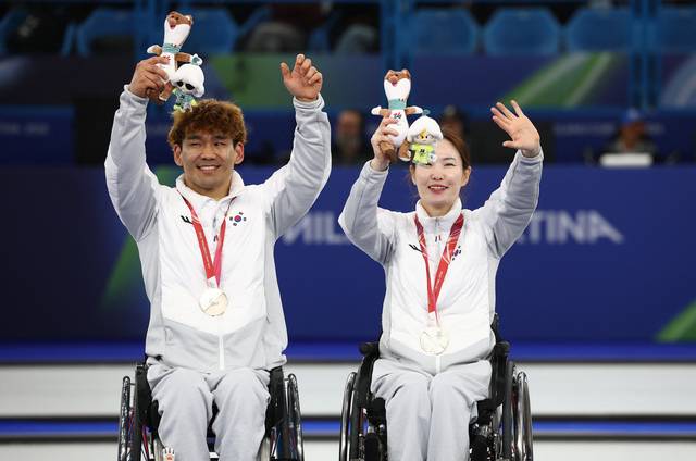 백혜진(오른쪽)과 이용석이 12일(한국시간) 이탈리아 코르티나담페초의 코르티나 올림픽 컬링 스타디움에서 열린 2026 밀라노·코르티나 동계패럴림픽 휠체어컬링 믹스더블 시상식에서 카메라를 향해 손을 흔들고 있다. 로이터 연합뉴스