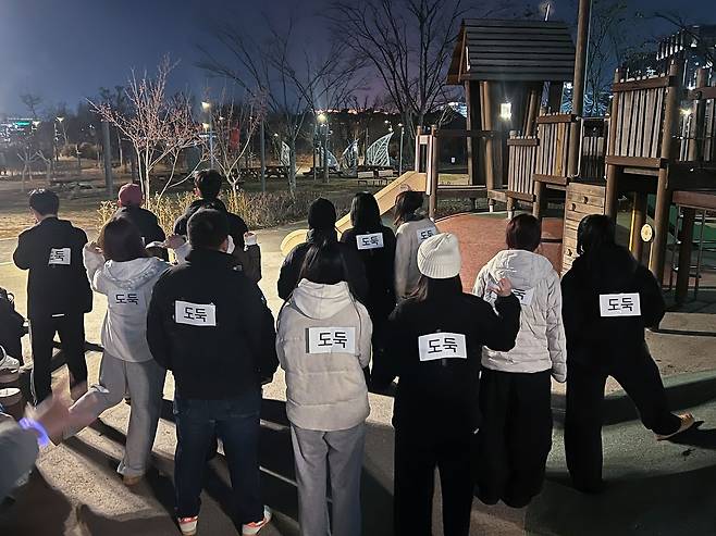 서울 강서구 서울식물원 잔디밭에서 열린 '경찰과 도둑' 놀이 참여를 위해 모인 사람들. 도둑 역할을 맡은 사람들이 등에 '도둑' 표시 종이를 붙이고 있다. 연합뉴스