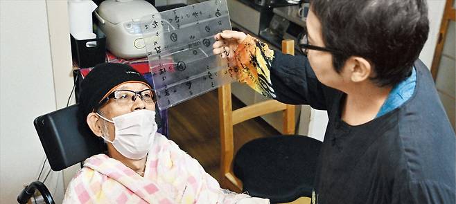 재택 돌봄 日 전신마비 환자… 문자판 통해 소통 일본 후쿠오카시의 자택에서 뇌출혈로 전신마비가 된 야베 아키히로(63·왼쪽)씨가 투명 문자판을 통해 아내 다카쿠라 미에(61)씨와 소통하고 있는 모습. /마이니치신문