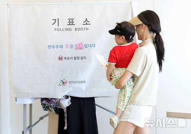 [서울=뉴시스 홍효식 기자 = 한국의 6·3 지방선거 결과에 대해 일본 언론은 여당의 승리로 평가하며, 이재명 대통령이 유권자들로부터 긍정적인 평가를 받고 있다고 진단했다. 다만 서울시장 선거에서 국민의힘 후보가 승리한 데 대해선 '타격'이라는 평가도 나왔다. 사진은 제9회 전국동시지방선거일인 지난 3일 서울 광진구 기아자동차 대공원대리점에 마련된 능동 제3투표소에서 한 유권자가 아이를 안고 기표소로 향하고 있는 모습. 2026.06.04. yesphoto@newsis.com