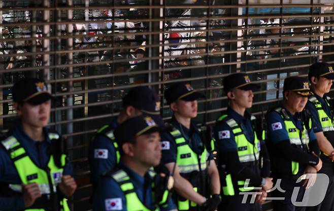 6일 오전 서울 송파구 올림픽공원 핸드볼경기장 개표소를 지키는 경찰 뒤로 6·3 지방선거 투표용지 부족 사태에 반발한 시민들의 모습이 창에 비치고 있다. 2026.6.6 ⓒ 뉴스1 구윤성 기자
