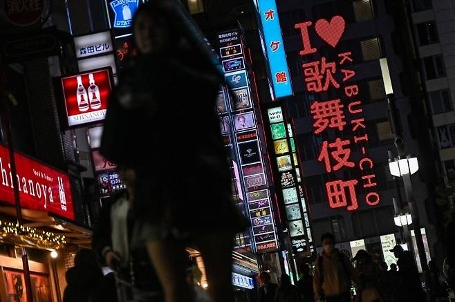도쿄 신주쿠구 가부키초의 홍등가 유흥가에 있는 네온사인 옆을 걷는 사람들의 모습. AFP 연합뉴스