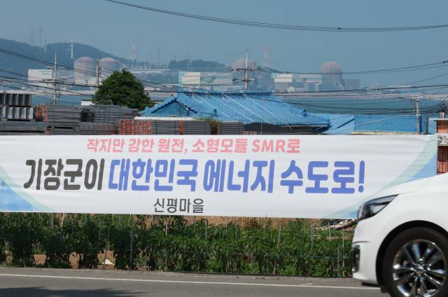 한국수력원자력이 신규 원전 건설을 위한 후보 부지로 대형원전 2기는 경북 영덕군, SMR 1기는 기장군을 확정했다고 밝힌 가운데 18일 부산 기장군 신평마을회관 인근 도로변에 내걸린 SMR 기장군 유치를 희망하는 내용의 현수막 뒤로 고리 1, 2, 3, 4호기가 보인다. 연합뉴스