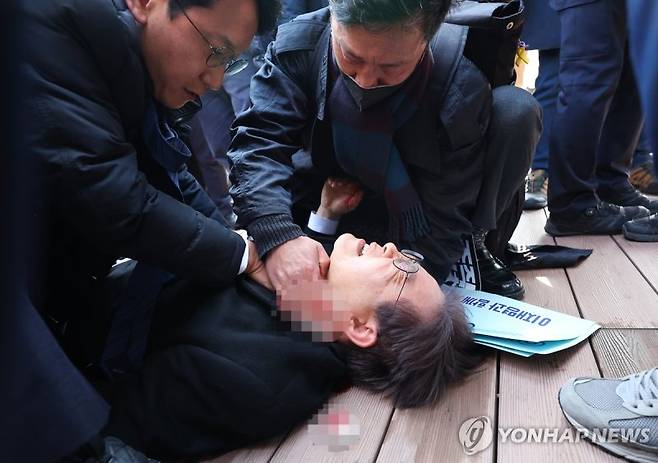 지난 2024년 1월 더불어민주당 이재명 대표가 부산 가덕도 신공항 부지를 둘러본 후 기자들과 문답을 진행하던 중 왼쪽 목 부위에 습격을 당해 피를 흘린 채 쓰러져 있다. 연합뉴스