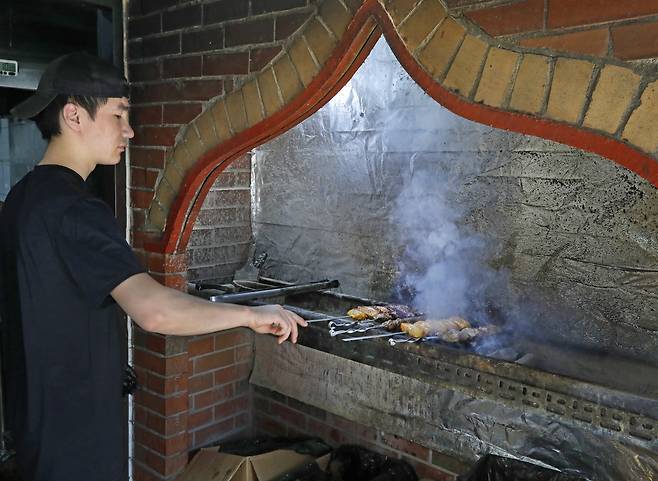 A person grills shashlik (grilled meat skewers) over a grill outside an Uzbek restaurant on Central Asia Street. PARK SANG-MOON