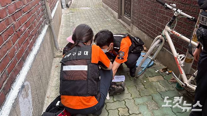 지난달 25일 오후 3시 30분쯤 할머니가 골목길에 쓰러져있다는 신고를 받고 출동한 구급대원들이 쪼그려 앉아 할머니의 상태를 살피고 있다. 김수정 기자