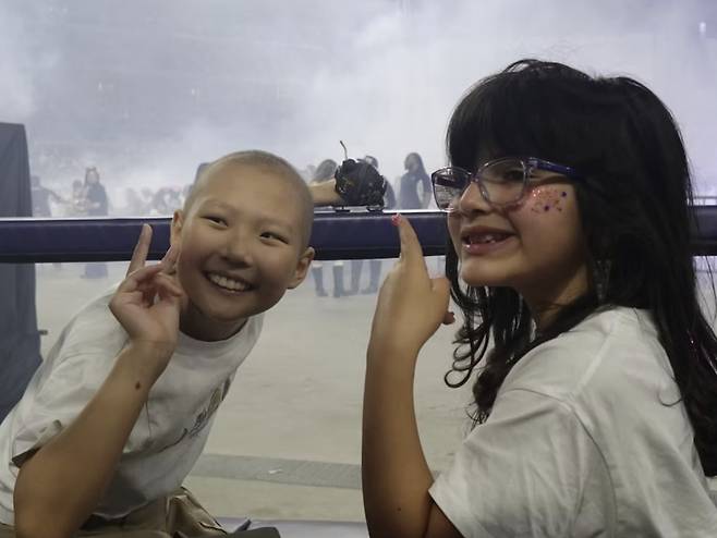 Olivya, à esquerda, e uma criança com câncer curtem o show da turnê mundial "Arirang" do BTS em Arlington, Texas, no dia 15 de agosto. HERÓIS PARA CRIANÇAS