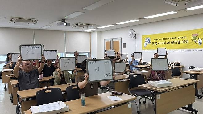 9월2일 경기도 수원 광교노인복지관에서 열린 ‘2026 시니어 디지털 금융교육’에 참여한 수강생들이 AI를 배우는 다짐 등을 적은 칠판을 머리 위로 들어올리고 있다. 카카오임팩트재단 제공.