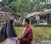 지진으로 파괴된 집 앞에 서 있는 인도네시아인들